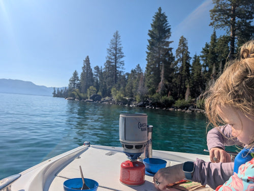 The Backpacker stove cooking on the bow of a boat on Lake Tahoe with a child beside it