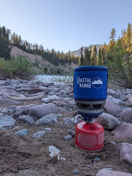 The Backpacker stove running on a rocky riverbank in golden evening light