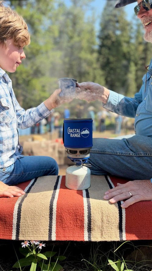 Child and grandfather share steaming mugs beside the Coastal Range Backpacker stove
