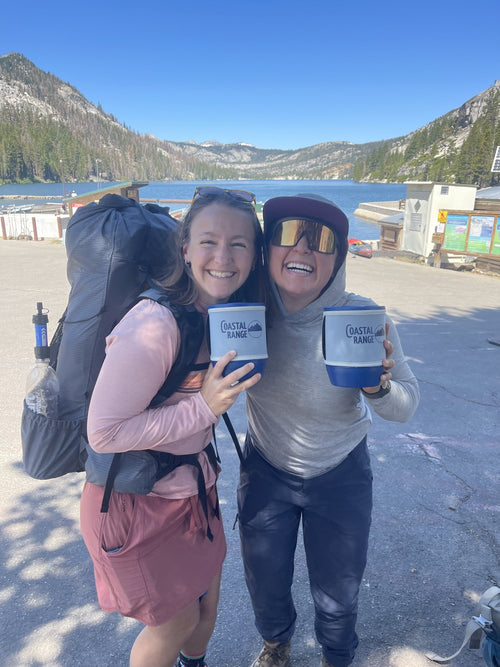 Two backpackers wearing full packs hold Coastal Range Backpacker cooking pots at a mountain trailhead