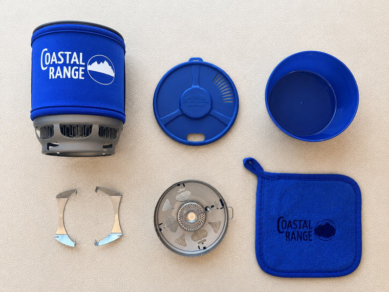 Flat lay of everything included with the Coastal Range Backpacker: pot, strainer lid, bowl, pot supports, burner, and microfiber cleaning towel.