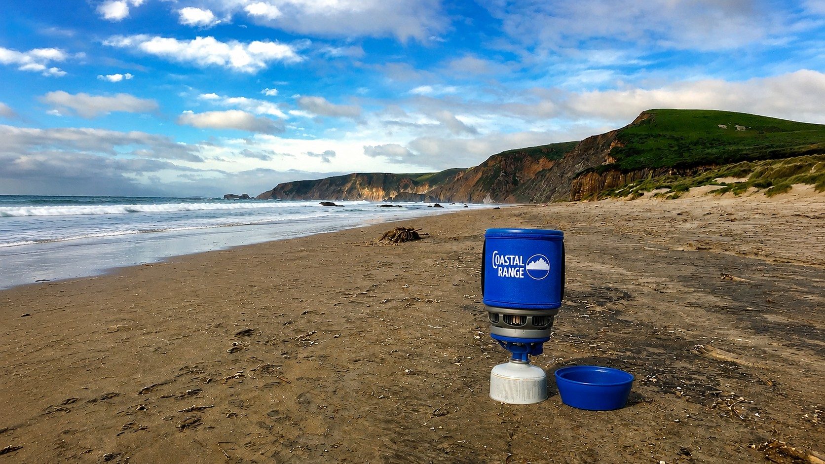 The Backpacker camping stove on a sunny California beach with coastal cliffs behind