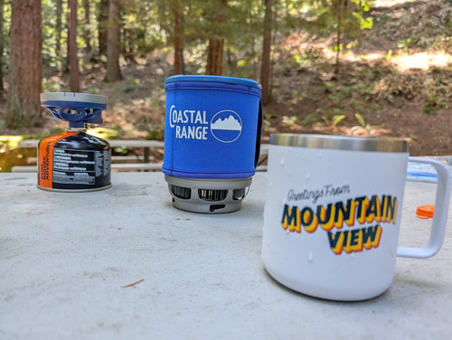 The Backpacker stove on a picnic table in a redwood forest next to a camp mug