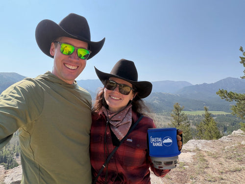 A smiling couple in cowboy hats at a high-country overlook holding the Backpacker