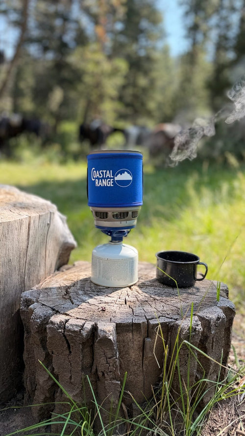 The Backpacker steaming on a tree stump with animals grazing beyond